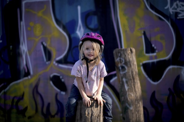 Little girl, 3 years, blonde, climbing, post, climbing facility, climbing frame, in front of wall full of graffiti, helmet, playground, Stuttgart, Baden-Württemberg, Germany, Europe
