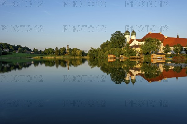Romanesque Benedictine abbey Seeon monastery, monastery church St. Lambert with reflection in the monastery lake, calm smooth water in the evening light at sunset, behind the side church Maria zu Breuhausen, also Bräuhausen, Seeon-Seebruck, Chiemgau, Upper Bavaria, Bavaria, Germany, Europe