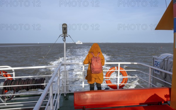 Norderney, Lower Saxony, Germany - The ferry Frisia IV operated by AG Reederei Norden-Frisia sails from Norderney to Norddeich. Norderney is one of the East Frisian Islands in the North Sea. In front, a woman in a winter coat stands at the railing and looks out to sea