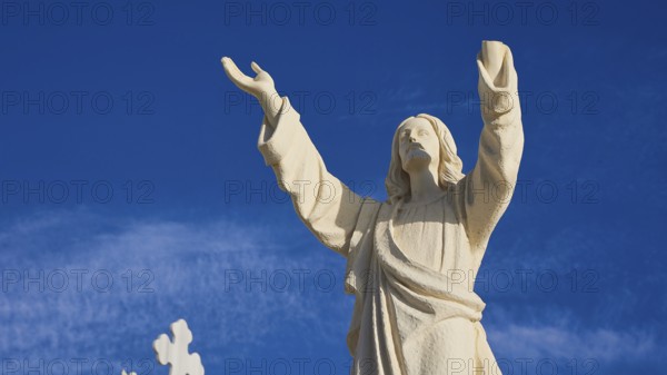 A stone statue of Jesus with outstretched arms against a blue sky, Agios Nikolaos church, cemetery, Pigadia, town and harbour, Pigadia Bay, main town, Karpathos, Dodecanese, Greek Islands, Greece, Europe
