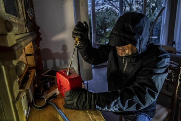 Symbolic image of a burglary, perpetrator has broken into a flat from the garden side and is looking for loot, breaks open a cash box, valuables, money