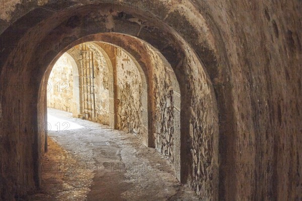 An old, dark tunnel with stone walls and a glow of light at the end, Venetian Sea Fortress, Leper Island, Spinalonga, Elounda Bay, Mirabello Bay, East Crete, Crete, Greek Islands, Greece, Europe