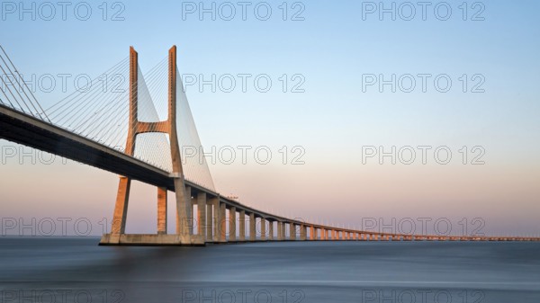 A long cable-stayed bridge spans over water under a gradient sunset sky, Lissabon, Vasco Da Gama-Brücke