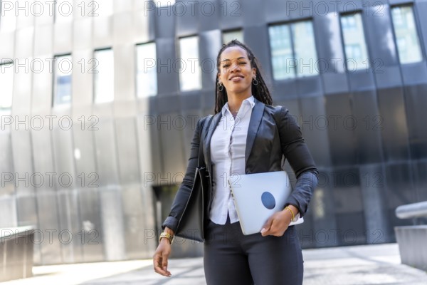 Professional young latin businesswoman standing carrying laptop in the city next to a modern financial building