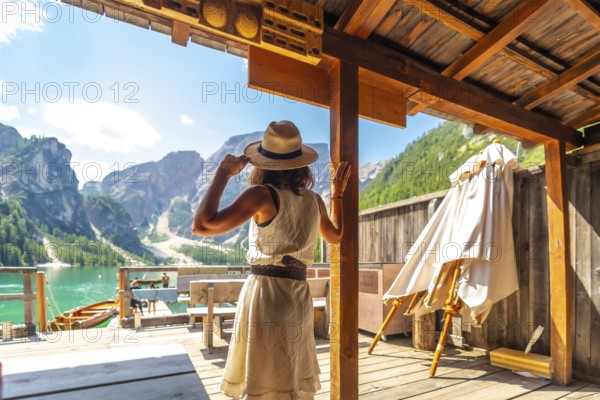 Woman wearing straw hat enjoying stunning panorama of lake braies, also known as pragser wildsee, in the heart of the dolomites, a unesco world heritage site