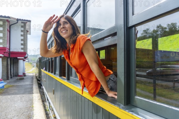 A woman in an orange shirt is looking out the window of a train. The train is yellow and green