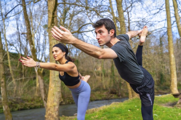 Yoga teachers performing a balancing asana by a river in the forest, enjoying the benefits of outdoor practice