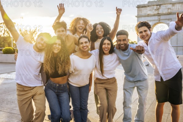 Portrait of diverse group of cheerful young people having fun and raising arms while standing through the city