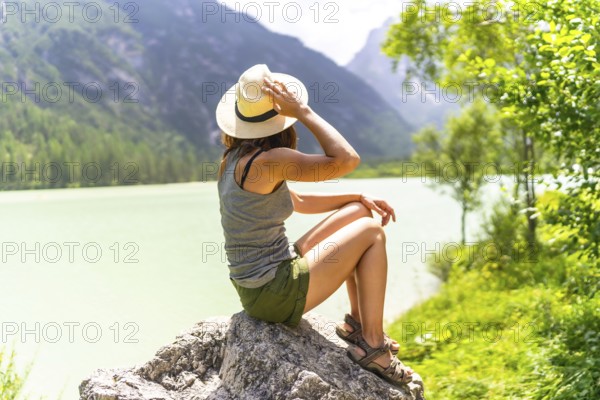Young woman enjoying the view of the turquoise water of lago di landro, also called durrensee lake, in the dolomites, italy, during summer holidays