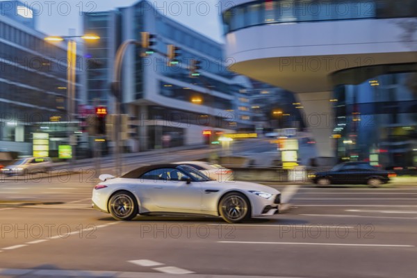 Car at night in front of urban surroundings with modern architecture, pull-along. Mercedes-Benz SL Roadster AMG. Stuttgart, Baden-Württemberg, Germany, Europe