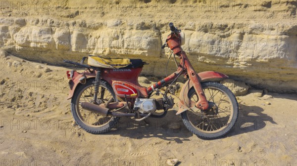 An old Honda C50 motorbike stands abandoned in front of a rocky cliff, Paralia Agios Theodoros beach, Arkasa, Karpathos, Greece, Europe