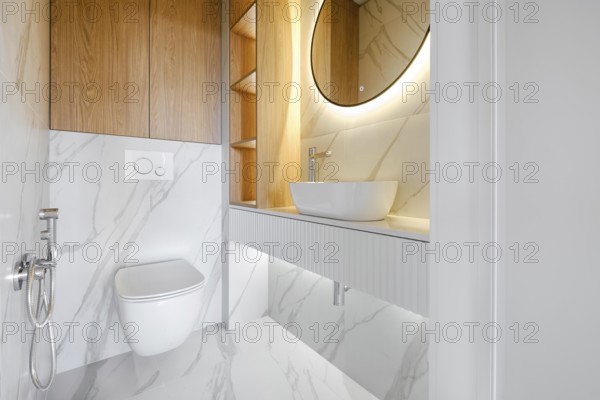 This contemporary bathroom showcases minimalistic design with marble walls and a circular mirror, emphasizing clean lines. A wall-mounted toilet and vessel sink add to the sophisticated aesthetic