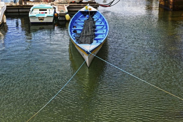 A blue fishing boat with a net lies quietly in a sunny harbour, small town of Vila Franca do Campo, Sao Miguel, Azores, Portugal, Europe