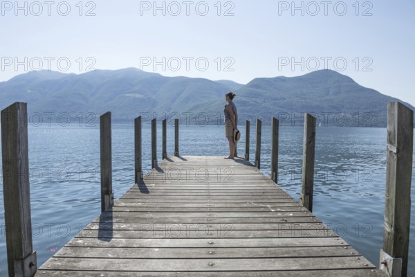 Woman Standing on a Pier on Lake Maggiore with Mountain in a Sunny Day in Brissago, Ticino, Switzerland, Europe
