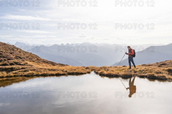 Mountaineer hiking with poles, reflected in a small mountain lake on the Krahberg, mountain panorama in autumn, Venet crossing, Ötztal Alps, Tyrol, Austria, Europe