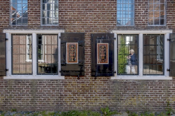 Facade of a brick building with mullioned windows and dark shutters, reflections in the glass, Hindeloopen, province of Friesland, Netherlands