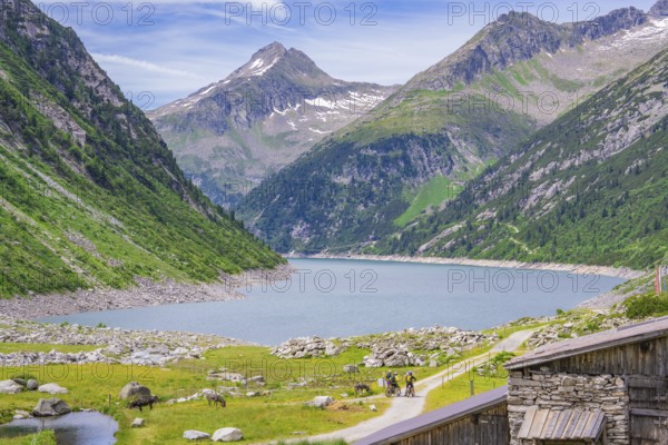 Scenery of mountains with a lake and two cyclists on a path, green nature and blue sky, Klein Tibet, Zillertal, Austria, Europe