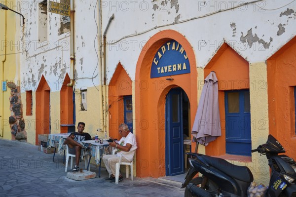 People sitting in front of a colourful facade of a taverna and enjoying their time on the street, Mandraki, Nisyros, Dodecanese, Greek Islands, Greece, Europe