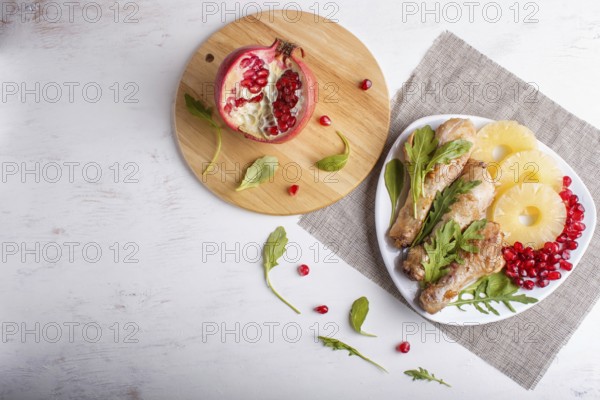 Fried chicken legs with rucola, pineapple and pomegranate seeds on white wooden background, copy space, top view