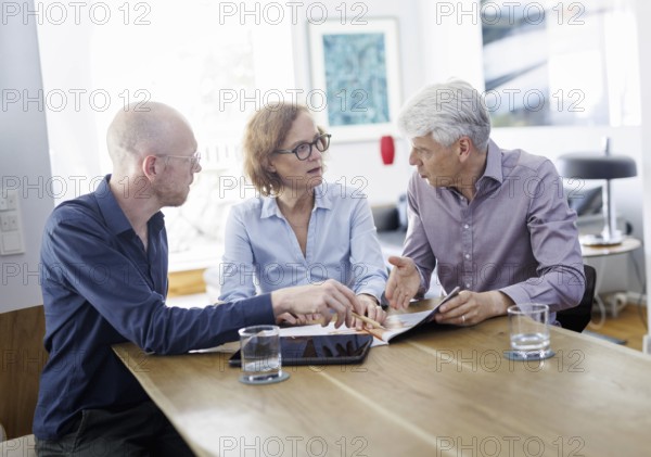 Symbolic photo on the subject of counselling. An older woman and an older man sit together at a table at home and receive counselling from a young man. Berlin, 13.08.2024