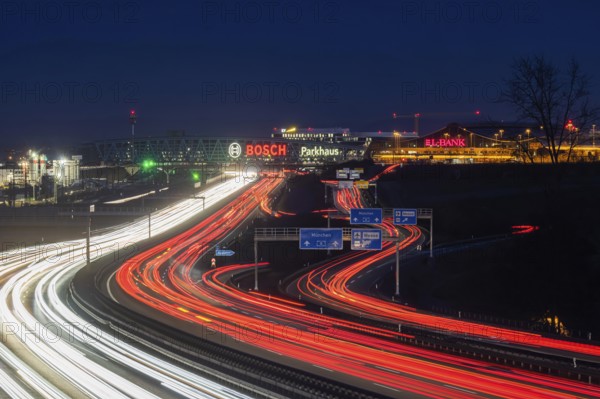 A8 motorway at Stuttgart Airport in the evening. Heavy traffic, lanes of light. Modern architecture of Messe Stuttgart with multi-storey car park above the motorway lanes. Logo of the Bosch company. Stuttgart, Baden-Württemberg, Germany, Europe