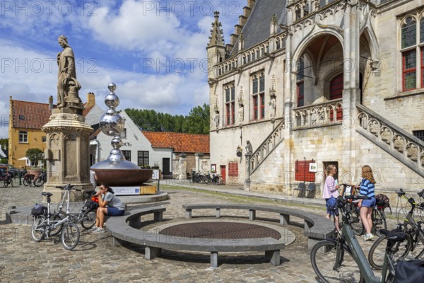 Statue of Jacob van Maerlant and cyclists in front of the Brabantine Gothic town hall in the city Damme in summer, West Flanders, Belgium, Europe