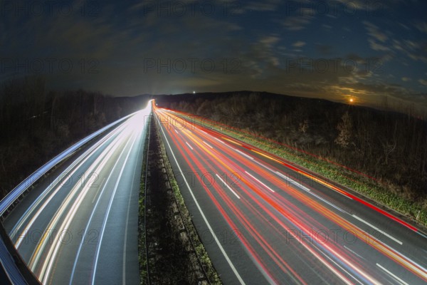 A7 Motorway, Autobahn, beside Kassel at night with light trails from the traffic headlights and taillights and the full moon rising in the distance, Hesse, Germany, Europe