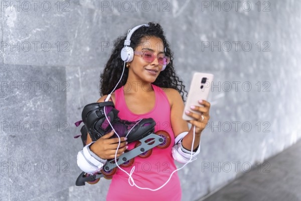 Latin beauty woman with inline skates listening to music with mobile phone and headphones at urban park