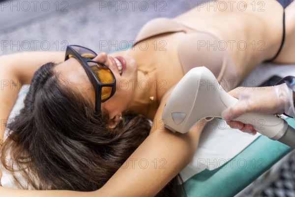 Woman in protect eyeglasses lying on a couch getting armpit laser hair removal procedure