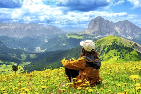 Woman hiker sitting in a vibrant flower field, admiring the stunning seceda peaks rising majestically in the dolomites of italy