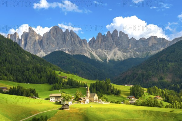 Green meadows, pine forests, and the iconic odle mountains rising majestically behind the church of santa maddalena in val di funes, italy