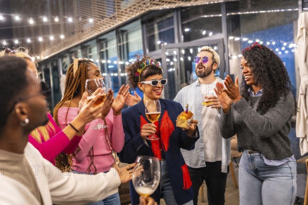 Multi-ethnic friends clasping and singing birthday song to a woman standing outside a night bar terrace