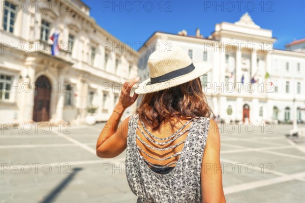 Tourist holding her straw hat admiring tartini square in piran, slovenia, during summer holidays