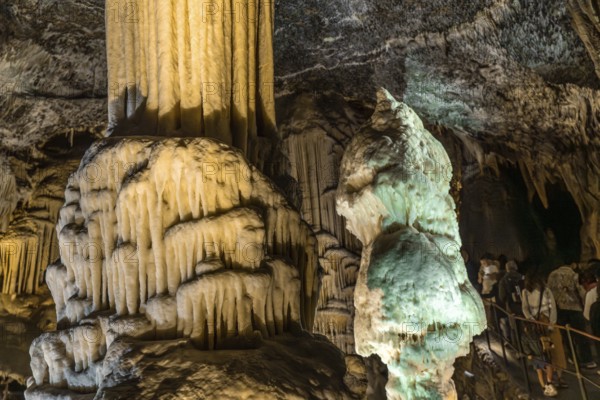 Tourists marveling at illuminated stalactites and stalagmites formations inside the famous postojna cave in slovenia, a popular tourist attraction