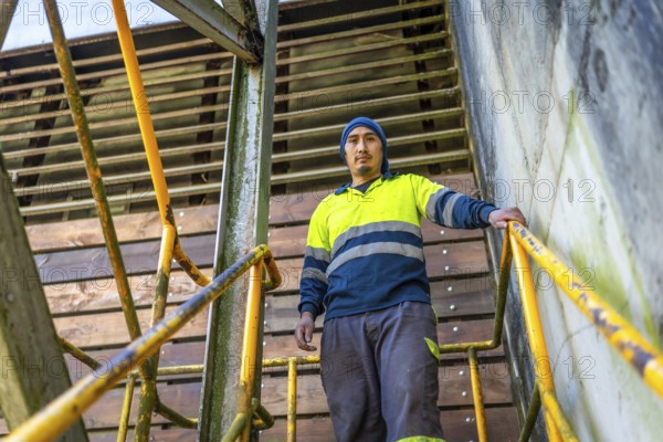 Low angle view portrait of a latin man with reflective clothes standing outside stairs in a recycling factory