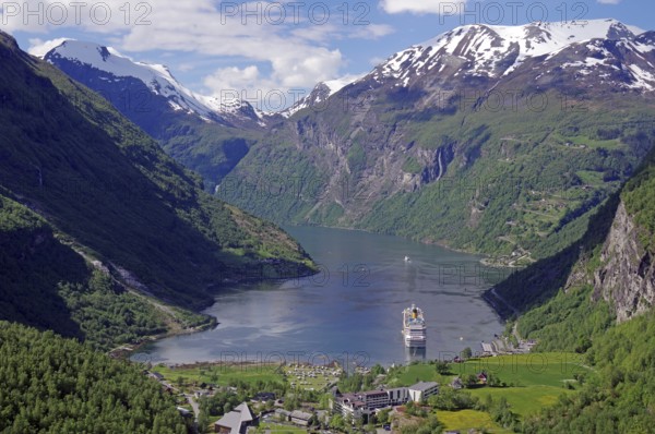 A fjord with a cruise ship surrounded by green mountains with snow-capped peaks under a blue sky with white clouds, Geirangerfjord, Fjordland, Norway, Europe