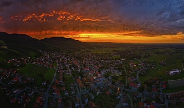A village under a dramatic sunset sky with glowing clouds and mountains in the background, Bad Feilnbach