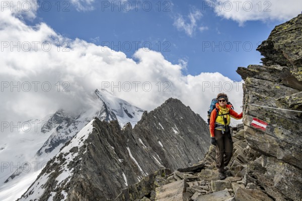 Mountaineer on a rocky path with safety rope and mountain panorama, glaciated summit Großer Möseler in the background, descent from the summit of Schönbichler Horn, Berliner Höhenweg, Zillertal Alps, Tyrol, Austria, Europe