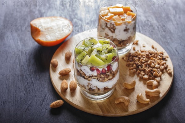 Dessert with greek yogurt, granola, almond, cashew, kiwi and persimmon on wooden background. close up