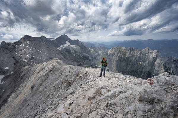 Mountaineer with helmet on a narrow rocky path, crossing the Jubiläumsgrat, view of Zugspitze and Höllental in steep rocky mountain landscape, ascent to Alpspitze via the south-west climb, Wetterstein range, Bavaria, Germany, Europe