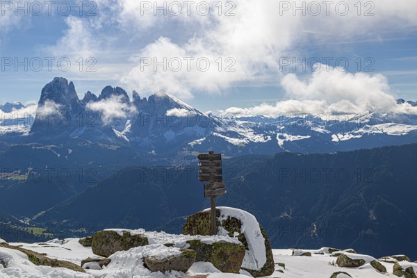 Snow-covered mountains under a blue sky with clouds and a wooden signpost with a view of the Lankofel mountain group in Val Gardena, South Tyrol, Italy, Europe