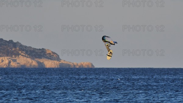 Wingfoiller, surfer in the air over the sea near a coast with cliffs, windsurfer, Meltemi windsurfing spot, Devils Bay, Paralia Vatha, Vatha Beach, southeast coast, Karpathos, Dodecanese, Greek Islands, Greece, Europe