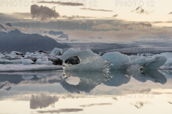 Icebergs reflected in calm water against a mountain backdrop, clouds, Jökulsárlón glacier lagoon or Jökulsarlon, South Iceland, Iceland, Europe