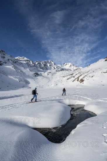 Small stream in a snow-covered mountain landscape, ski tourers in a valley, ascent to the Madritschspitze, Ortler Alps, Vinschgau, Italy, Europe