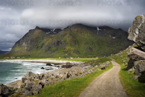 Uttakleiv (Utakleiv) with mountains, in the foreground the hiking trail around the mountain Veggen. Beach, rocks and sea on the left. Cloudy sky with sun. Early summer. Uttakleiv, Vestvagoya, Lofoten, Norway, Europe