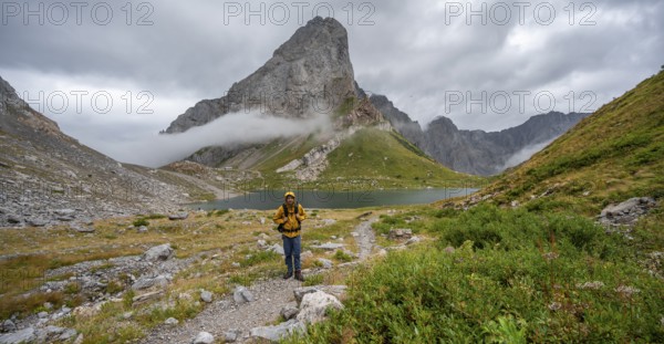 Mountaineers on a hiking trail with a view of rocky cloudy mountains and Wolayersee, hiking trail to Wolayerseehütte, cloudy mountain peaks, Carnic Alps, Carnic High Trail, Carinthia, Austria, Europe