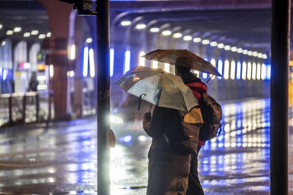 Illuminated subway at the main railway station, pedestrians at a pedestrian crossing, rainy weather, city centre, in the evening, Essen, North Rhine-Westphalia, Germany, Europe