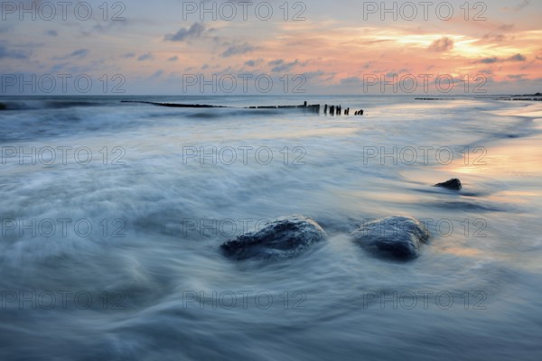 Sunset on the beach, boulders and old groyne in the surf, Klintholm Havn, Møn Island, Denmark, Europe