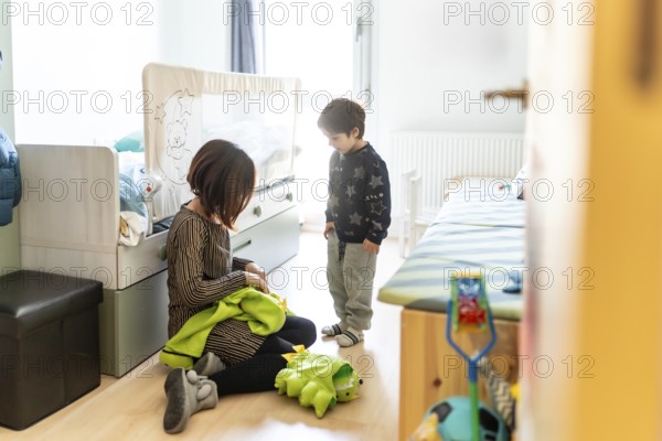 Mother and son playing together at home, preparing a dinosaur costume for a fun game in their bedroom