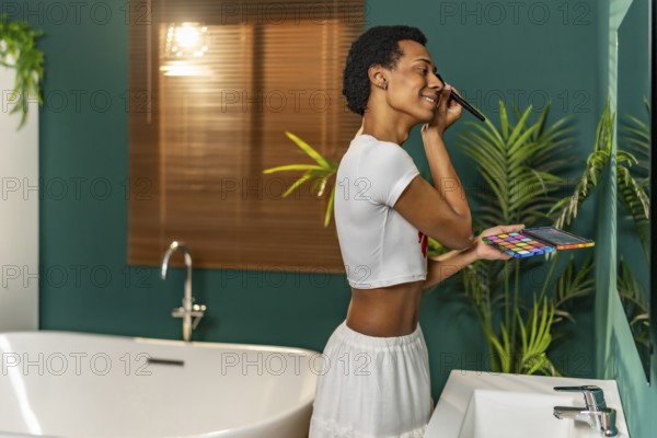 Gay latin man applying make up standing facing bathroom mirror at home